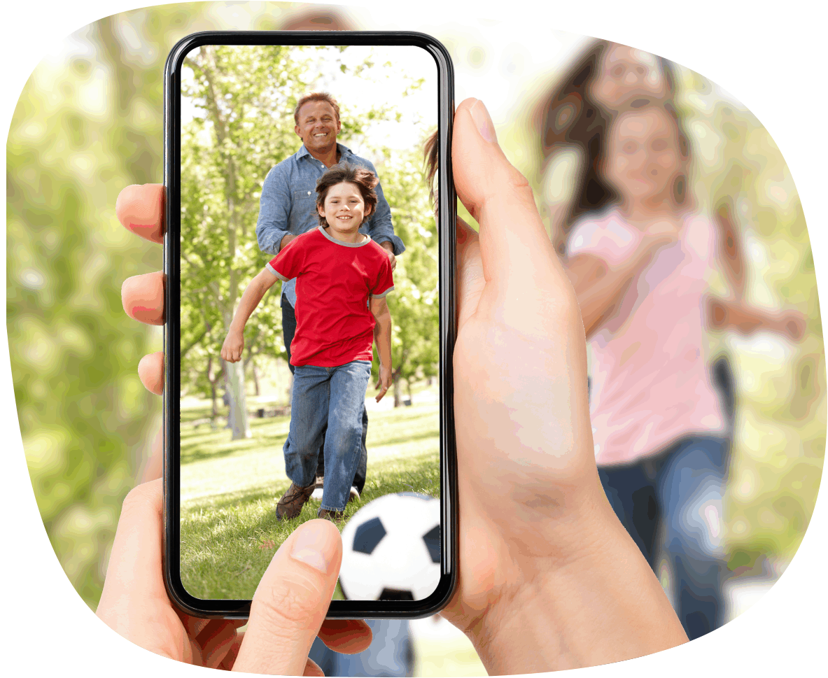 Mit einem Smartphone fotografiert jemand eine Familie beim Fußballspielen im Freien.